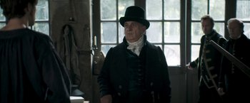 Movie still from “Lost Illusions” (2021), directed by Xavier Giannoli – An older man wearing a black hat and a black coat; Medium shot, Low angle