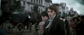 Movie still from “Lost Illusions” (2021), directed by Xavier Giannoli – Two young men dressed in period clothing standing next to each other in front of a horse drawn carriage; Medium shot, Low angle