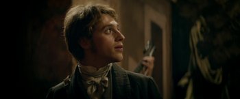 Movie still from “Lost Illusions” (2021), directed by Xavier Giannoli – A young man holding a gun while wearing a bow tie; Close Up shot, Over the shoulder angle