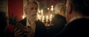 Movie still from “Lost Illusions” (2021), directed by Xavier Giannoli – An old man smoking a cigarette in front of a group of candles; Medium shot, Over the shoulder angle