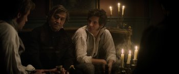 Movie still from “Lost Illusions” (2021), directed by Xavier Giannoli – A man sitting next to another man in front of candles; Medium shot, Over the shoulder angle