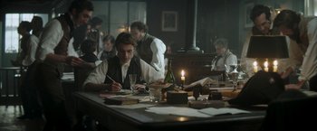 Movie still from “Lost Illusions” (2021), directed by Xavier Giannoli – A man sitting at a table writing on a piece of paper; Medium shot, High angle