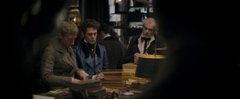 Movie still from “Lost Illusions” (2021), directed by Xavier Giannoli – A group of people sitting around a table with books on top of it; Medium shot, Over the shoulder angle