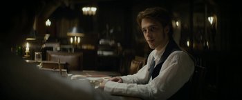 Movie still from “Lost Illusions” (2021), directed by Xavier Giannoli – A man sitting at a table in front of a laptop computer; Medium shot, Over the shoulder angle