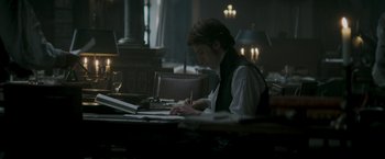 Movie still from “Lost Illusions” (2021), directed by Xavier Giannoli – A man sitting at a table writing on a piece of paper; Medium shot, Over the shoulder angle