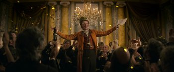 Movie still from “Lost Illusions” (2021), directed by Xavier Giannoli – A man holding a bottle of champagne in front of a group of people; Medium shot, Low angle