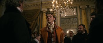 Movie still from “Lost Illusions” (2021), directed by Xavier Giannoli – A man in a suit and a crown in front of a chandelier; Medium shot, Low angle