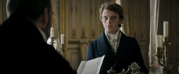 Movie still from “Lost Illusions” (2021), directed by Xavier Giannoli – A young man sitting in front of a table with candles; Medium shot, Over the shoulder angle