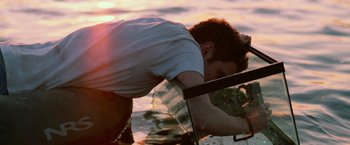 Movie still from “Lost River” (2014), directed by Ryan Gosling – A man in a white t - shirt is in the water; Medium shot, Over the shoulder angle