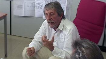 Movie still from “Lost in La Mancha” (2002), directed by Louis Pepe – An older man sitting in a chair talking to someone; Medium shot, Over the shoulder angle