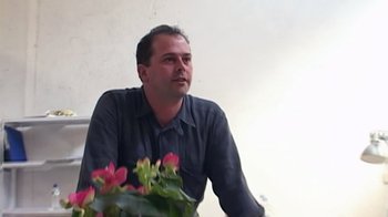 Movie still from “Lost in La Mancha” (2002), directed by Louis Pepe – A person sitting in front of a flower pot; Close Up shot, Low angle