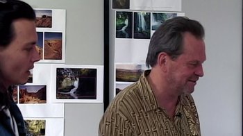 Movie still from “Lost in La Mancha” (2002), directed by Louis Pepe – A man standing in front of a wall of pictures; Medium shot, Over the shoulder angle