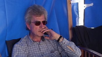 Movie still from “Lost in La Mancha” (2002), directed by Louis Pepe – An older man wearing sunglasses is sitting in a chair; Close Up shot, High angle