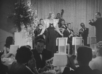 Movie still from “Love Affair” (1939), directed by Leo McCarey – An old black and white photo of a woman singing; Wide shot, Low angle