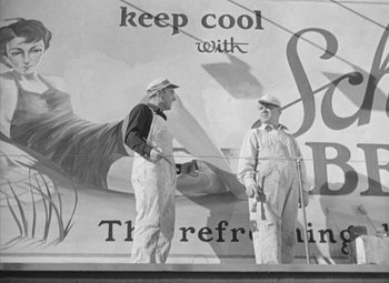 Movie still from “Love Affair” (1939), directed by Leo McCarey – Two men standing next to each other in front of an advertisement; Wide shot, Low angle