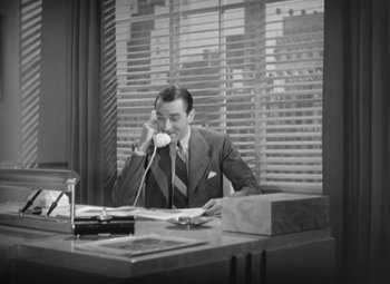 Movie still from “Love Affair” (1939), directed by Leo McCarey – A man sitting at a desk talking on a phone; Medium shot, High angle