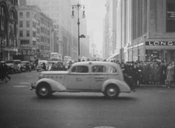 Movie still from “Love Affair” (1939), directed by Leo McCarey – An old car driving down a street past a crowd of onlookers; Extreme Wide shot, High angle