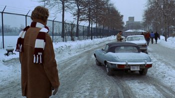 Movie still from “Love Story” (1970), directed by Arthur Hiller – A man is standing on the side of the road next to a car; Wide shot, High angle