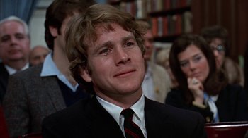 Movie still from “Love Story” (1970), directed by Arthur Hiller – A man in a black suit and a red striped tie; Close Up shot, Over the shoulder angle