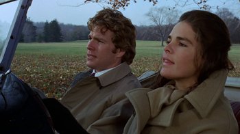 Movie still from “Love Story” (1970), directed by Arthur Hiller – A man and a woman sitting next to each other in a field; Close Up shot, Low angle