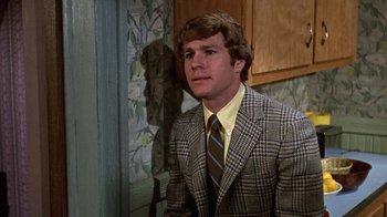Movie still from “Love Story” (1970), directed by Arthur Hiller – A man wearing a suit and tie in a kitchen; Close Up shot, Over the shoulder angle