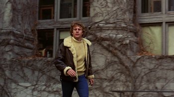 Movie still from “Love Story” (1970), directed by Arthur Hiller – A man in a brown jacket walking in front of a building; Medium shot, Low angle