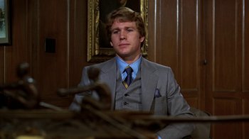 Movie still from “Love Story” (1970), directed by Arthur Hiller – A man in a suit and tie sitting in front of a painting; Medium shot, Low angle