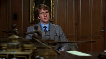 Movie still from “Love Story” (1970), directed by Arthur Hiller – A man sitting at a desk in a suit and tie; Medium shot, Low angle