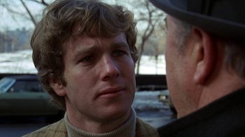 Movie still from “Love Story” (1970), directed by Arthur Hiller – A man in a sweater is talking to another man in a hat; Close Up shot, Over the shoulder angle