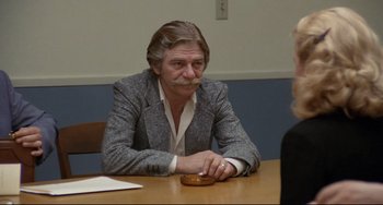 Movie still from “Love Streams” (1984), directed by John Cassavetes – A man sitting at a table with a donut in front of him; Medium shot, Over the shoulder angle