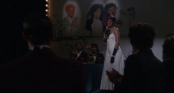 Movie still from “Love Streams” (1984), directed by John Cassavetes – A woman in a white dress is holding a microphone; Wide shot, Over the shoulder angle