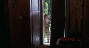 Movie still from “Love Streams” (1984), directed by John Cassavetes – A woman standing in a doorway holding flowers; Wide shot, Over the shoulder angle