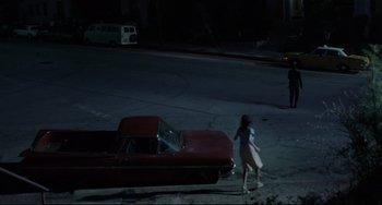 Movie still from “Love Streams” (1984), directed by John Cassavetes – A woman walking down a street past a red car at night; Extreme Wide shot, High angle