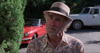 Movie still from “Love Streams” (1984), directed by John Cassavetes – An older man wearing a hat standing in front of a red car; Close Up shot, Over the shoulder angle
