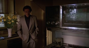 Movie still from “Love Streams” (1984), directed by John Cassavetes – A man in a suit standing next to a stove in a kitchen; Medium shot, High angle