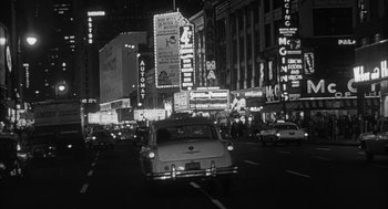Movie still from “Love with the Proper Stranger” (1963), directed by Robert Mulligan – A black - and - white photo of a car driving down a city street at night; Extreme Wide shot, High angle