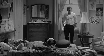 Movie still from “Love with the Proper Stranger” (1963), directed by Robert Mulligan – A black and white photo of a man standing in front of a bed; Wide shot, High angle