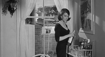 Movie still from “Love with the Proper Stranger” (1963), directed by Robert Mulligan – A black and white photo of a woman holding a wine bottle; Medium shot, Low angle