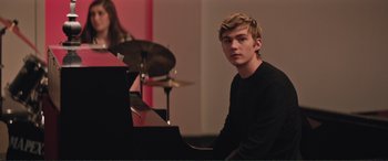 Movie still from “Love, Simon” (2018), directed by Greg Berlanti – A man sitting at a piano in front of drums; Medium shot, Over the shoulder angle