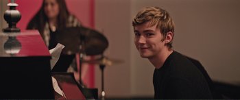 Movie still from “Love, Simon” (2018), directed by Greg Berlanti – A young man smiles while sitting in front of a drum set; Close Up shot, Over the shoulder angle