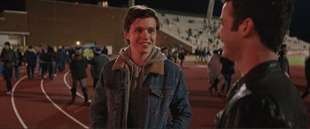 Movie still from “Love, Simon” (2018), directed by Greg Berlanti – A man in a denim jacket standing on a field; Close Up shot, Over the shoulder angle