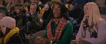 Movie still from “Love, Simon” (2018), directed by Greg Berlanti – A woman in a green shirt wearing a scarf and glasses is clapping at an event; Medium shot, Over the shoulder angle