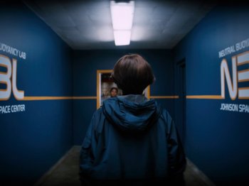 Movie still from “Lucy in the Sky” (2019), directed by Noah Hawley – A person standing in a hallway with a light shining on them; Medium shot, Over the shoulder angle