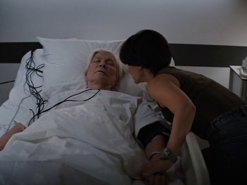 Movie still from “Lucy in the Sky” (2019), directed by Noah Hawley – An older man laying in a hospital bed with a young woman; Medium shot, High angle