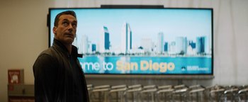 Movie still from “Lucy in the Sky” (2019), directed by Noah Hawley – A man standing in front of a large tv screen; Medium shot, Over the shoulder angle