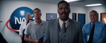 Movie still from “Lucy in the Sky” (2019), directed by Noah Hawley – A man in a suit and tie standing next to another man in a tie; Medium shot, Over the shoulder angle