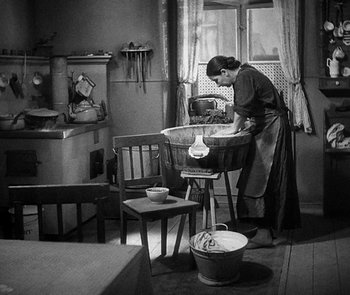 Movie still from “M” (1931), directed by Fritz Lang – An old photo of a woman washing dishes in a kitchen; Wide shot, High angle