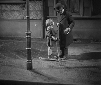 Movie still from “M” (1931), directed by Fritz Lang – An older man and a young girl on a scooter on the sidewalk; Wide shot, High angle