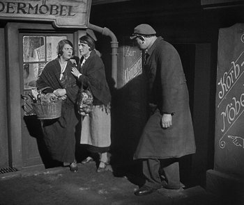 Movie still from “M” (1931), directed by Fritz Lang – Two women and a man stand in front of a building; Wide shot, Low angle