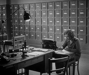 Movie still from “M” (1931), directed by Fritz Lang – A woman sitting at a table with a typewriter; Wide shot, High angle